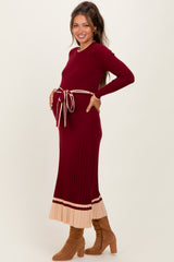 woman wearing a burgundy maternity dress with a tie waist and cream striped hem, showing her baby bump
