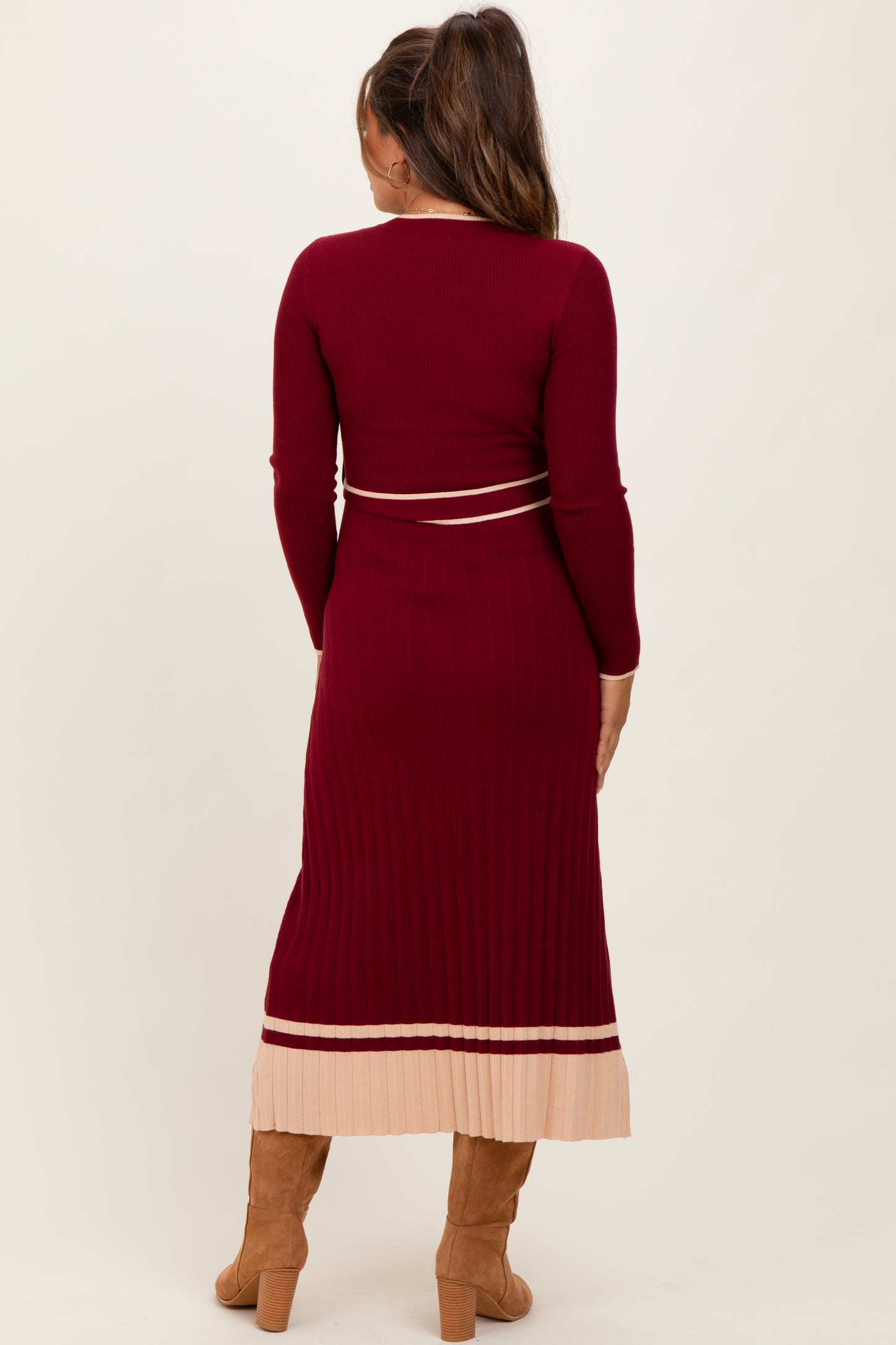 woman wearing a burgundy ribbed maternity dress with long sleeves and a pleated light pink hem