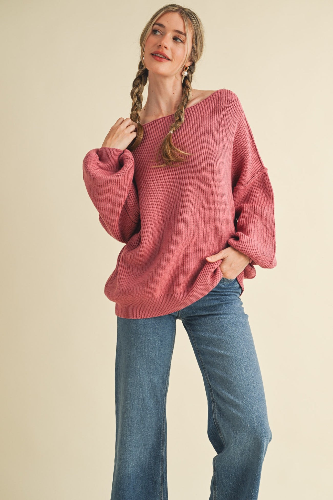 woman wearing a loose-fitting pink ribbed sweater and wide-leg blue jeans, posed with hands in pockets