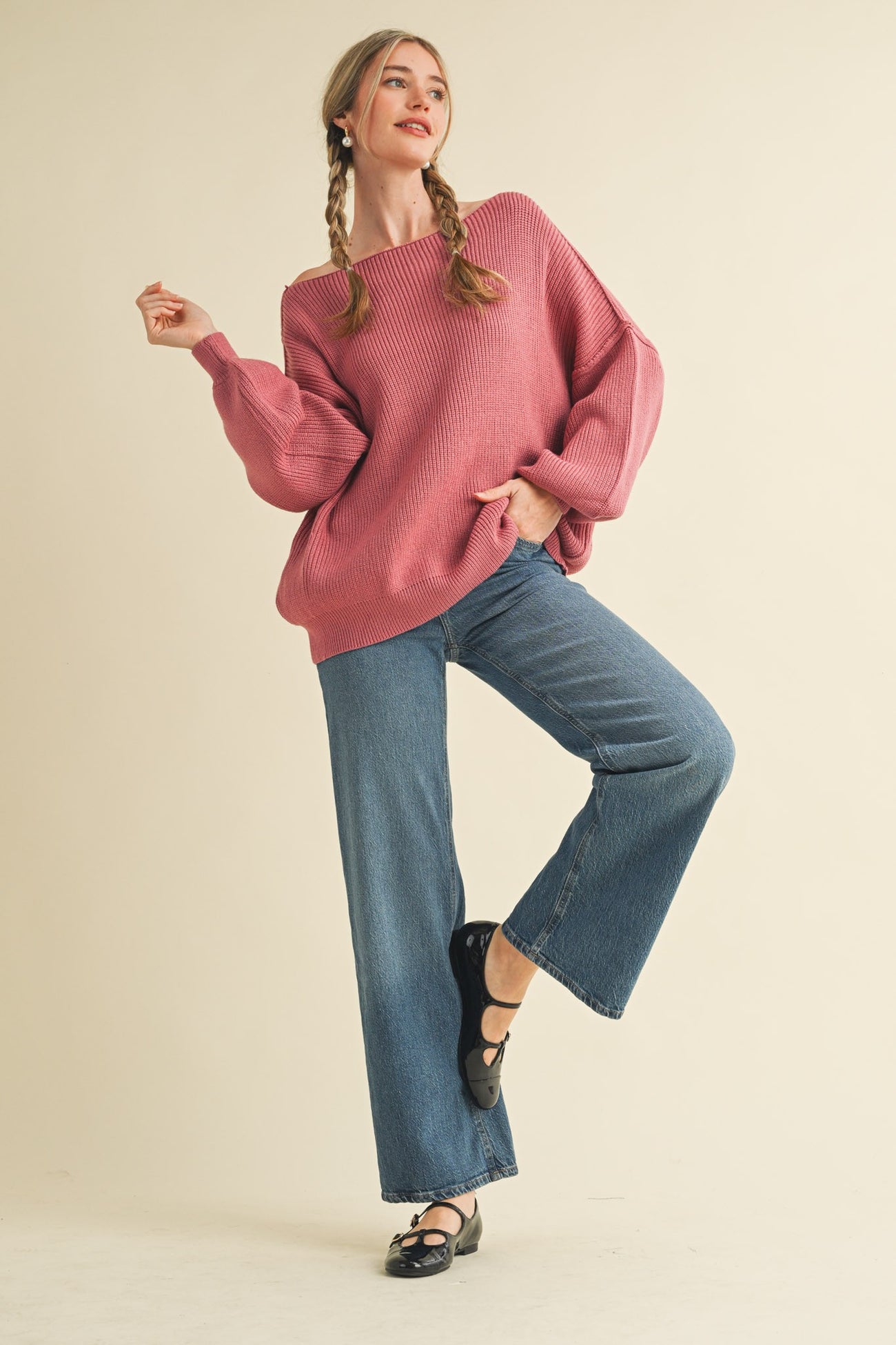 woman wearing a light pink oversized ribbed sweater and high-waisted flared jeans, striking a playful pose