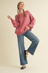 woman wearing a light pink oversized ribbed sweater and high-waisted flared jeans, striking a playful pose