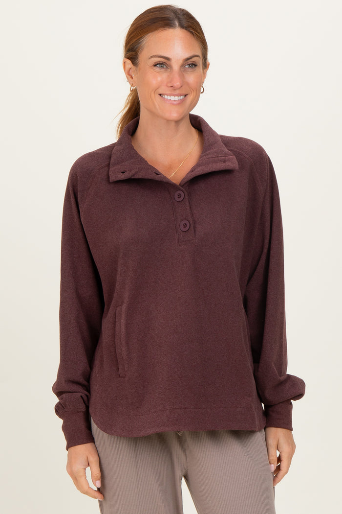 woman wearing a maroon pullover sweatshirt with a collar and button detail, featuring a front pocket