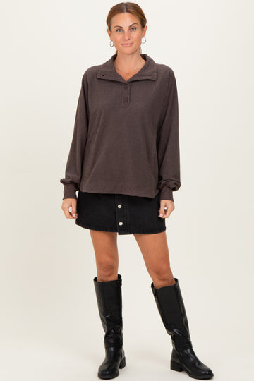 woman wearing a brown pullover sweatshirt with a collar and buttons, paired with a black denim skirt and black knee-high boots