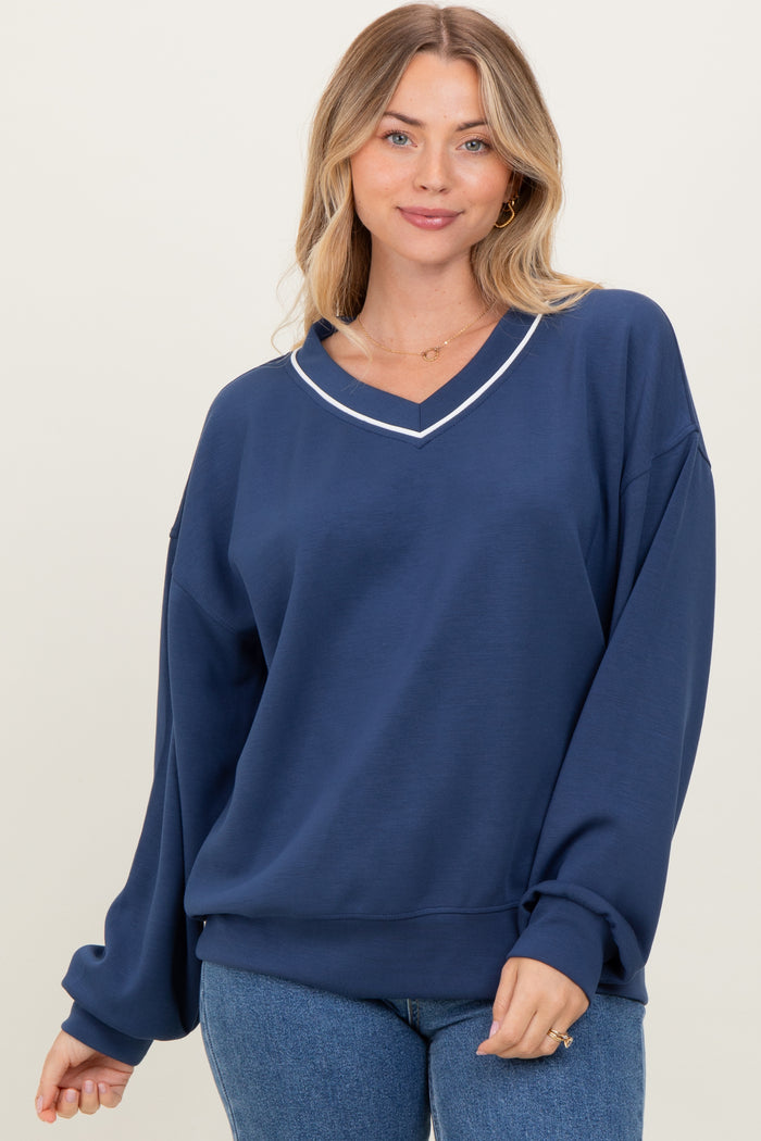 woman wearing a navy oversized sweatshirt with a v-neck and white trim details, posing casually