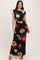 woman wearing a black off-shoulder floral maxi dress with colorful flowers and a fitted silhouette