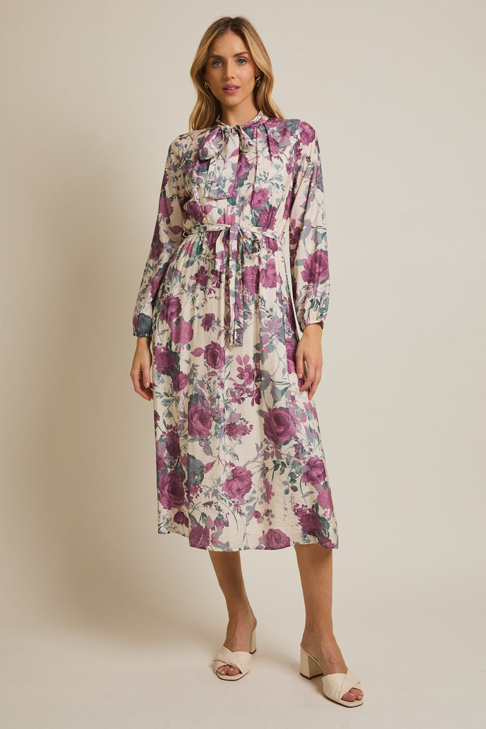 woman wearing a floral midi dress with purple and green flowers, tied at the waist, and sandals