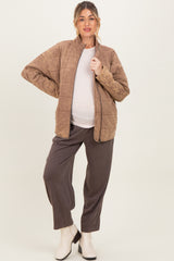 woman wearing a brown quilted maternity jacket over a gray top and black maternity pants, showing her baby bump