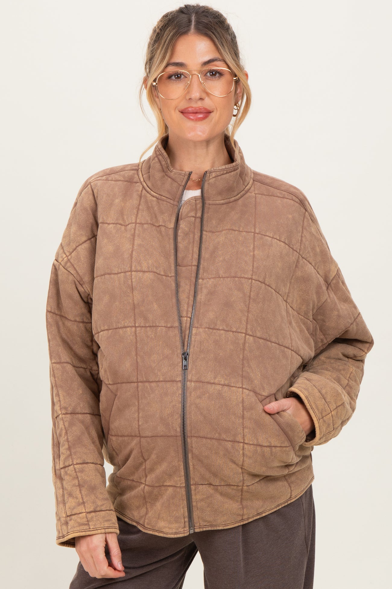 woman wearing a brown quilted maternity jacket with a zip front and side pockets, showing her baby bump