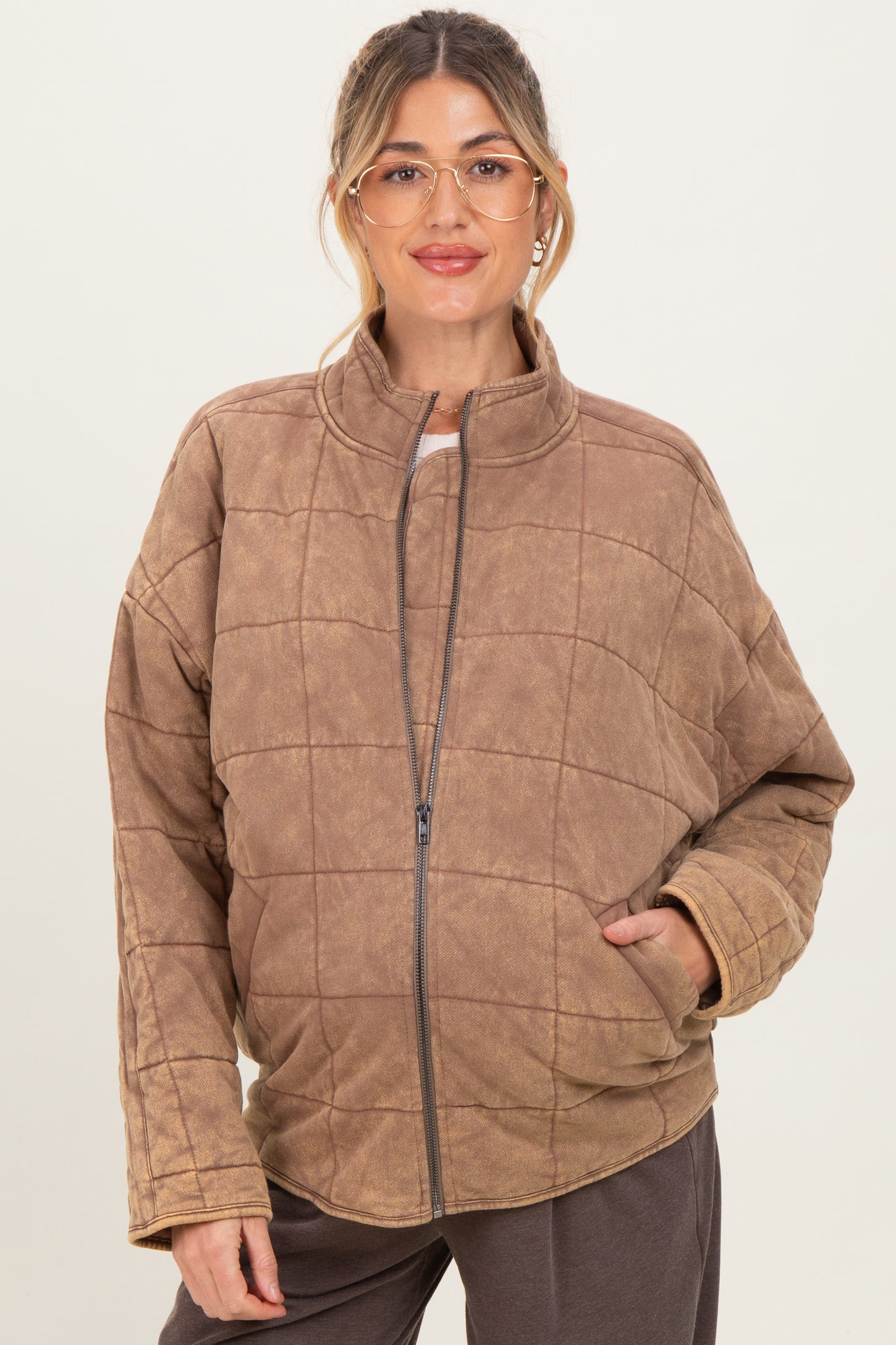 woman wearing a brown quilted maternity jacket with a zip front and side pockets, showing her baby bump
