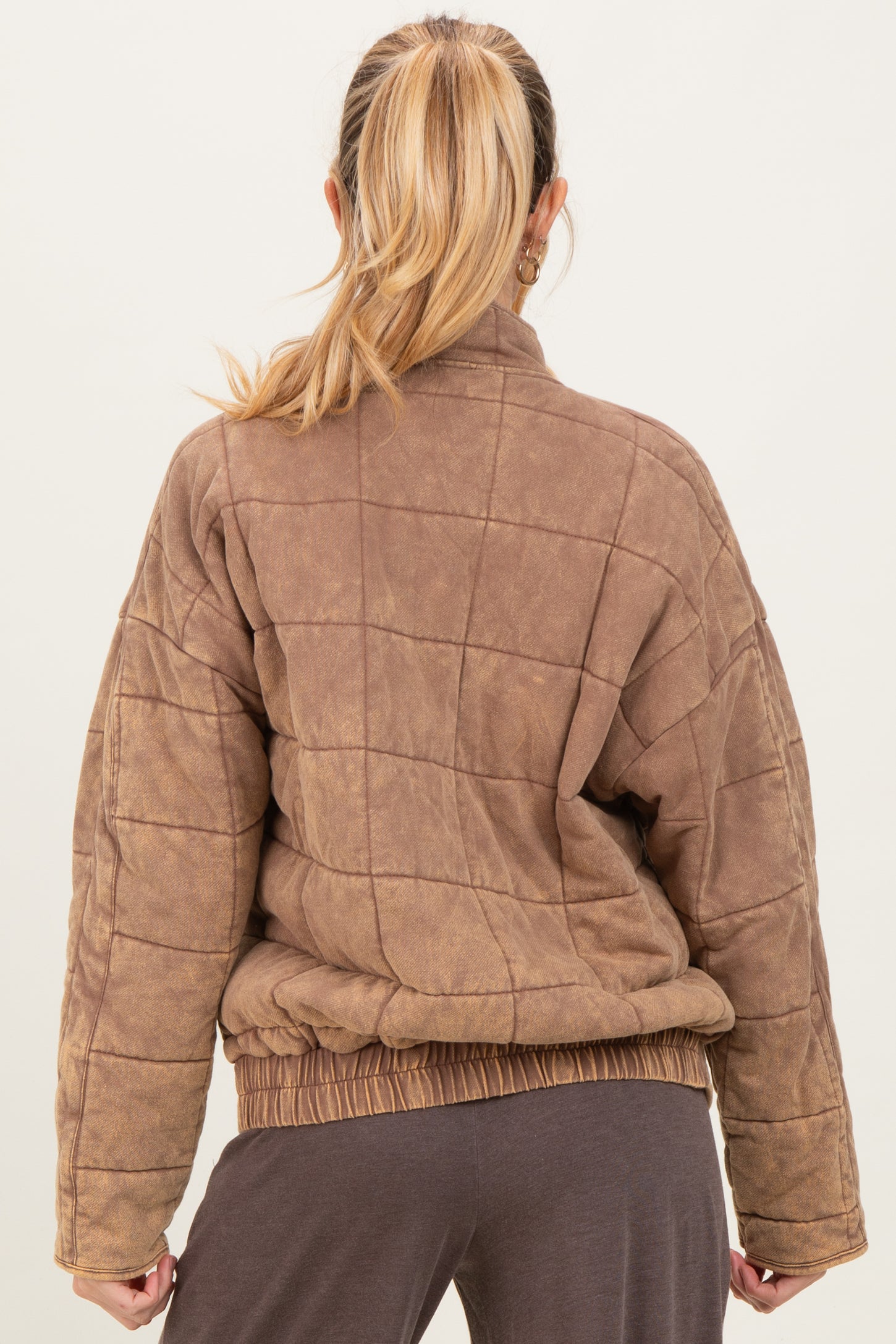 woman wearing a brown quilted maternity jacket with a relaxed fit and elastic hem, seen from the back