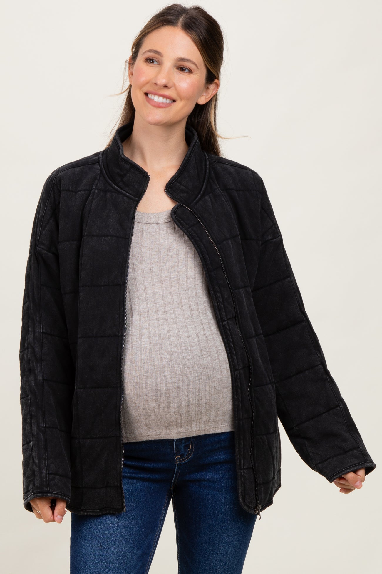 woman wearing a black quilted maternity jacket over a gray top, showcasing her baby bump while smiling