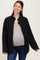 woman wearing a black quilted maternity jacket over a gray top, showcasing her baby bump while smiling