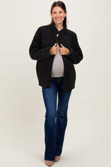 woman wearing a black quilted maternity jacket and a gray top, holding her baby bump while standing in flared jeans