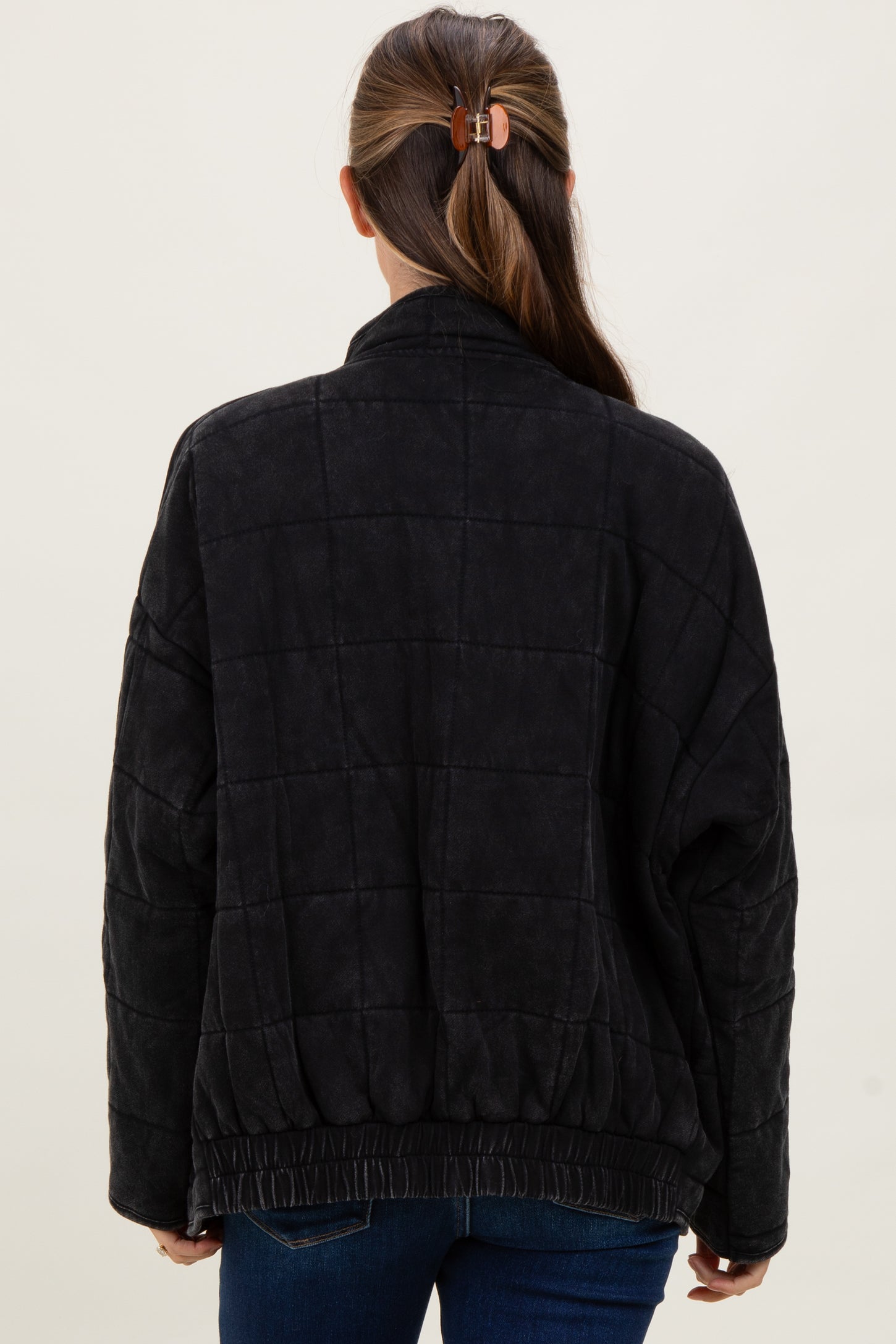 woman wearing a black quilted maternity jacket with a relaxed fit and elastic waistband, viewed from the back