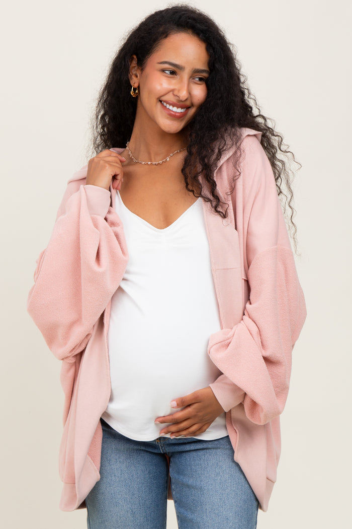 woman wearing a pale pink maternity hoodie over a white top and holding her baby bump while smiling