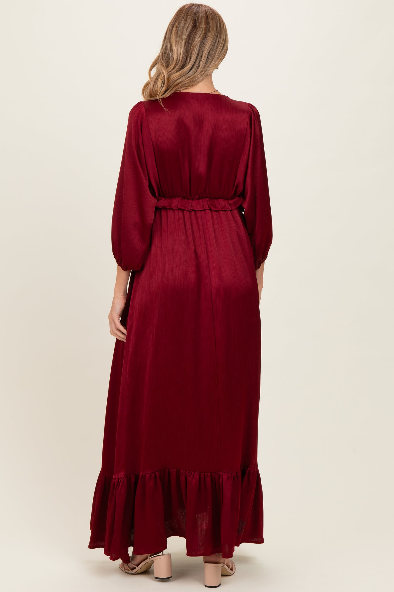 woman wearing a burgundy long sleeve maternity dress with a ruffled hem and belted waist, showing her baby bump