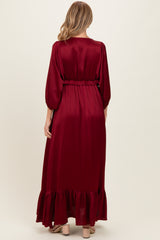 woman wearing a burgundy long sleeve maternity dress with a ruffled hem and belted waist, showing her baby bump