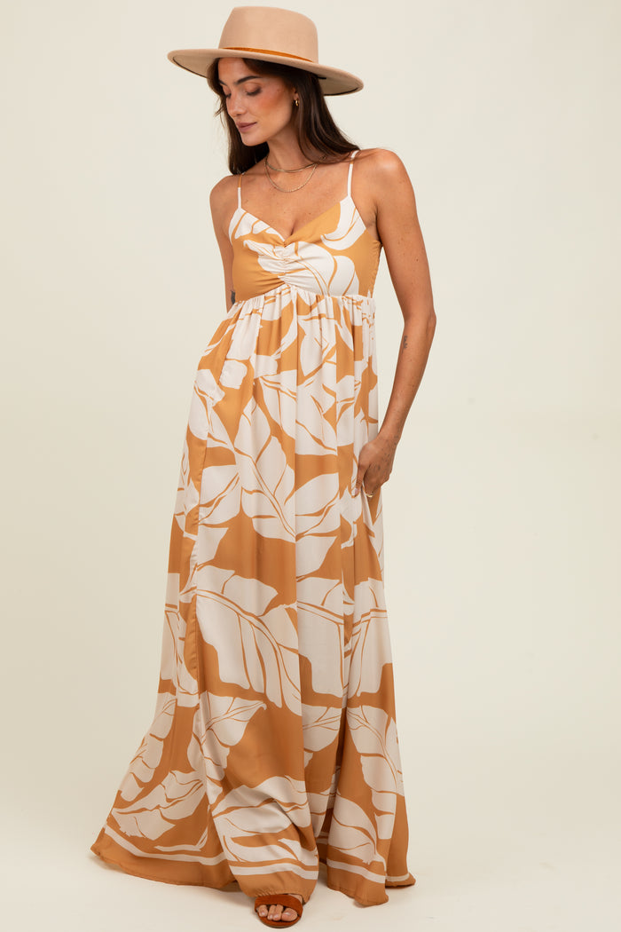 woman wearing a mustard yellow maxi dress with white leaf patterns and adjustable straps, paired with a wide-brimmed hat