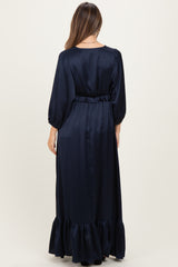 woman wearing a navy blue maternity maxi dress with long sleeves and a ruffled hemline, showing a baby bump from the back