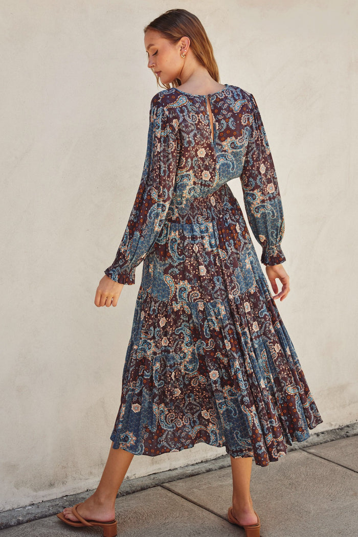 woman wearing a long sleeve bohemian floral maxi dress in shades of blue and burgundy, seen from the back