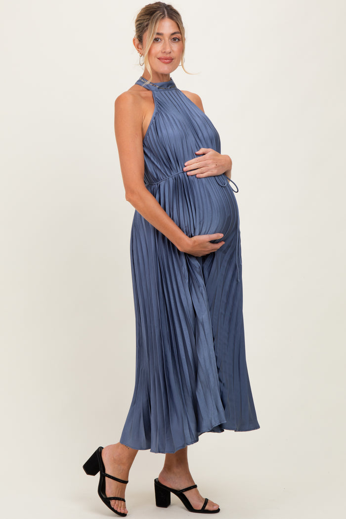 woman wearing a blue pleated maternity dress with a halter neck and holding her baby bump