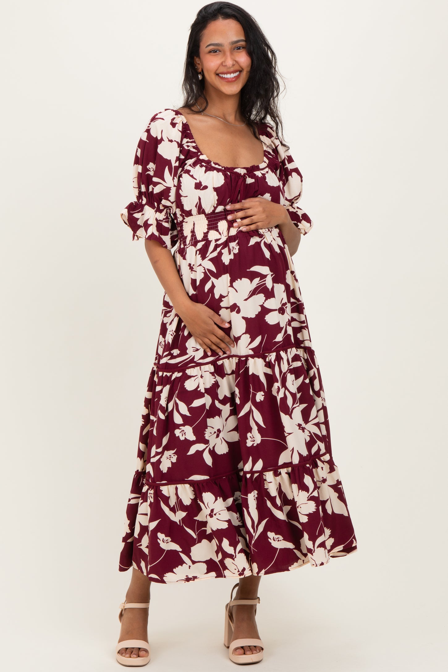 woman wearing a burgundy floral maternity dress with a tiered skirt and a square neckline, holding her baby bump