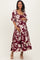 woman wearing a burgundy floral maternity dress with a tiered skirt and a square neckline, holding her baby bump