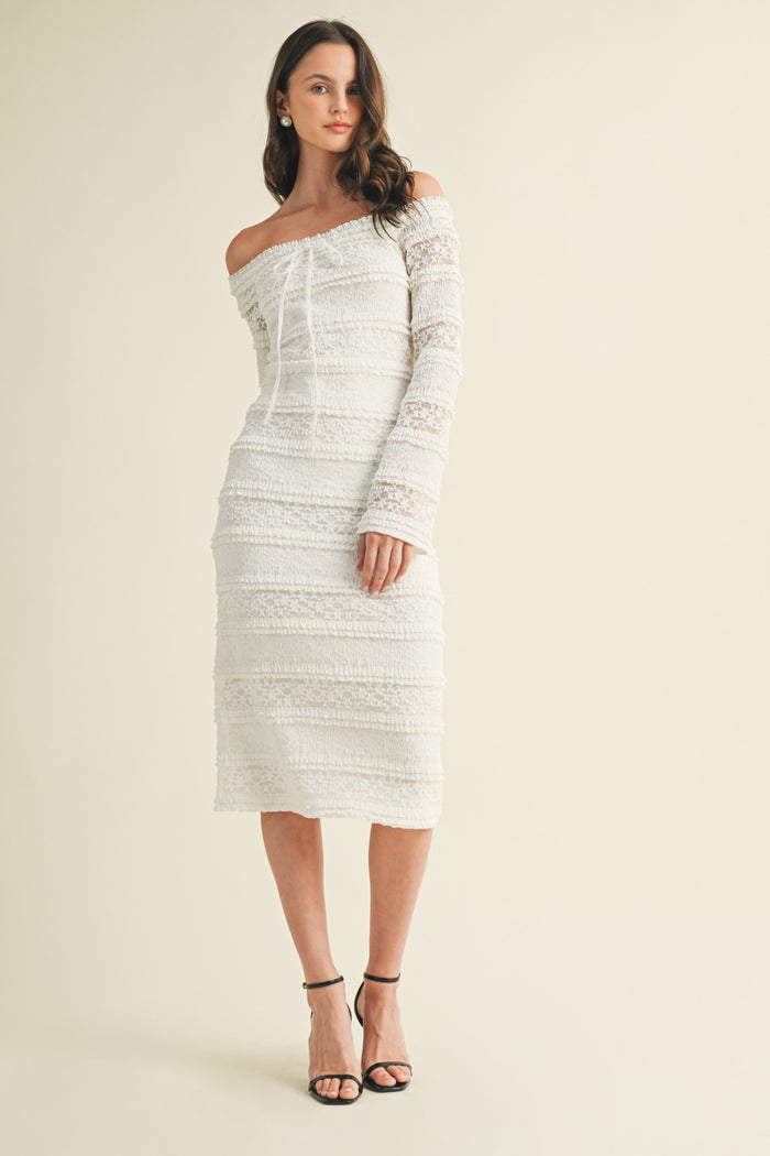 woman wearing a white off-the-shoulder midi dress with lace details and long puffed sleeve, standing in strappy heels