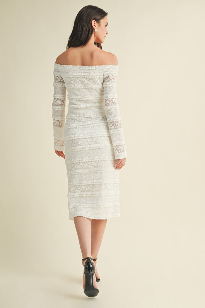 woman wearing a fitted off-the-shoulder white dress with long sleeves and a flared hem, seen from the back