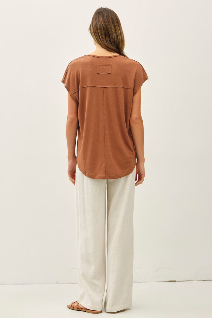 woman wearing a rust-colored short sleeve top with a back pocket and light beige wide-leg pants