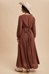 woman wearing a brown long sleeve maxi dress with tie back detail and a white cowboy hat