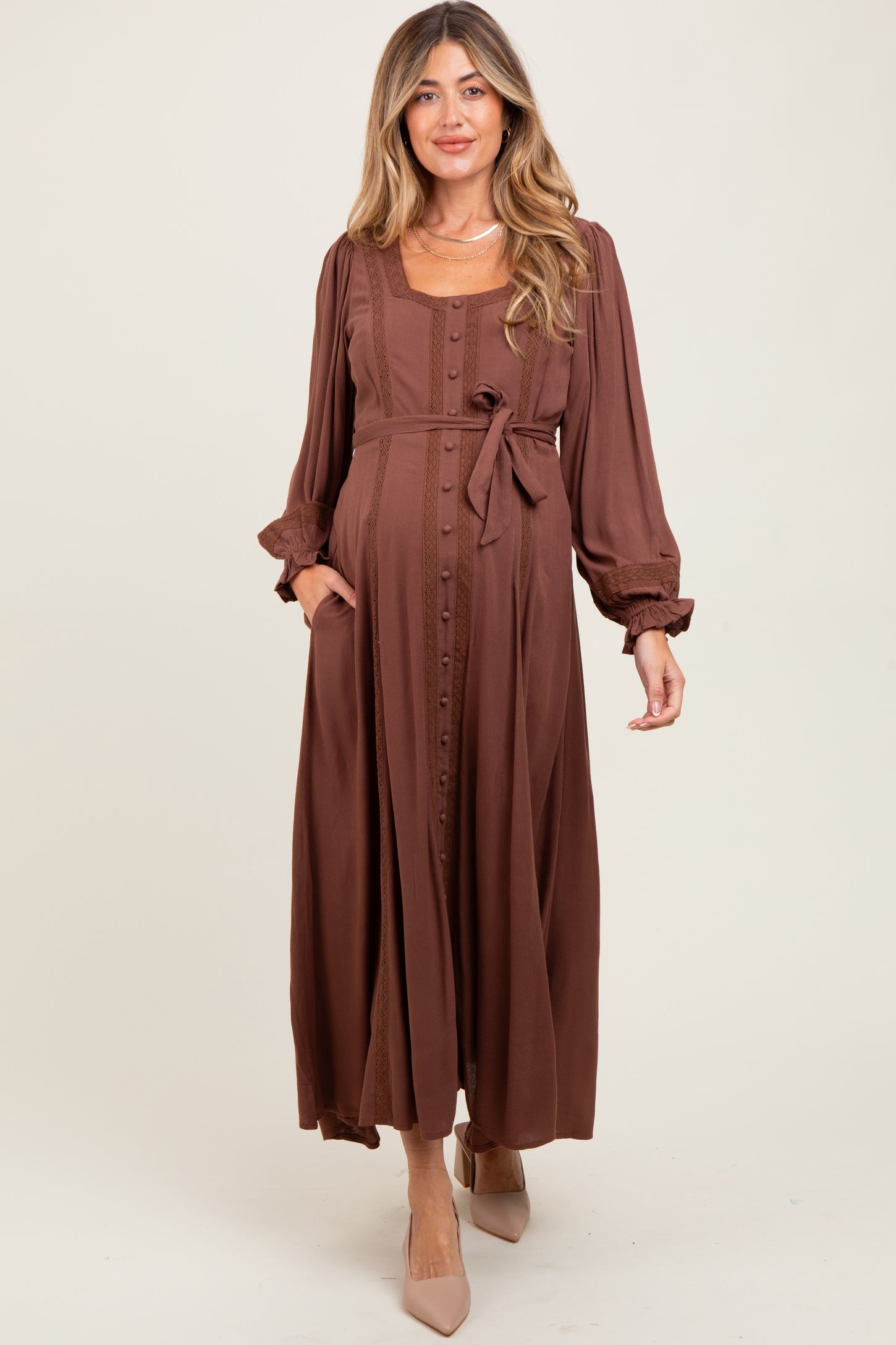 woman wearing a brown long sleeve maternity dress with buttons and a tie waist, featuring a relaxed fit and pockets