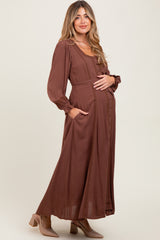 woman wearing a brown long sleeve maternity dress with buttons and pockets, showing her baby bump