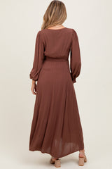 woman wearing a long brown maternity dress with long sleeves and a smocked waist, showing a flowing skirt