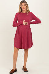 woman wearing a raspberry long sleeve maternity dress, holding her baby bump, with a flared skirt and ribbed texture