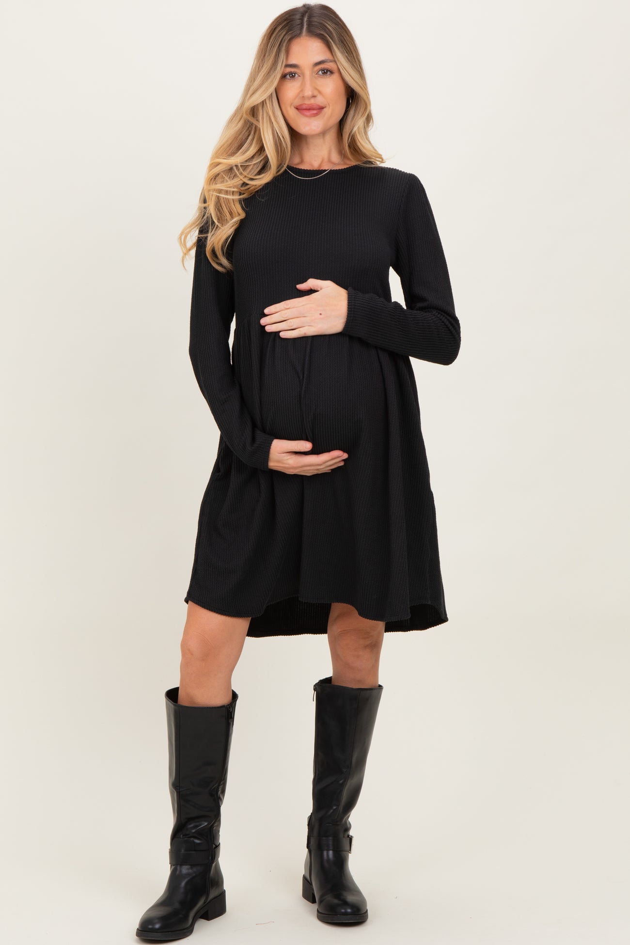 woman wearing a black ribbed maternity dress and holding her baby bump, paired with tall black boots