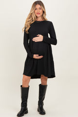 woman wearing a black ribbed maternity dress and holding her baby bump, paired with tall black boots