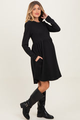 woman wearing a black long sleeve maternity dress with pockets and a baby bump, styled with knee-high black boots