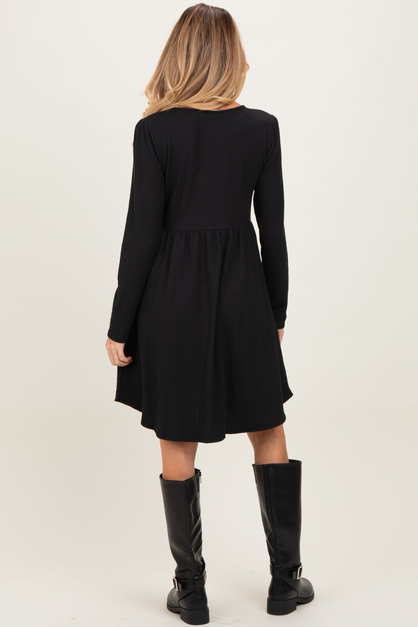woman wearing a black long sleeve maternity dress with a flared bottom, standing with her back to the camera