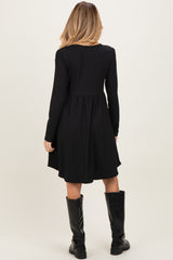 woman wearing a black long sleeve maternity dress with a flared bottom, standing with her back to the camera