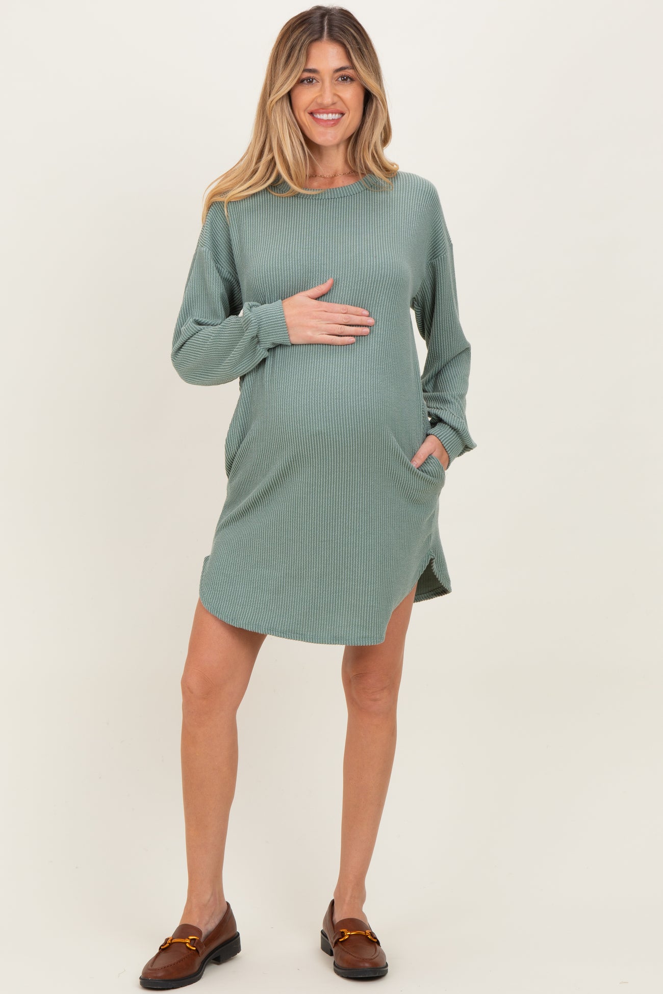 woman wearing a green striped maternity dress with long sleeves and pockets, holding her baby bump