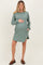 woman wearing a green striped maternity dress with long sleeves and pockets, holding her baby bump