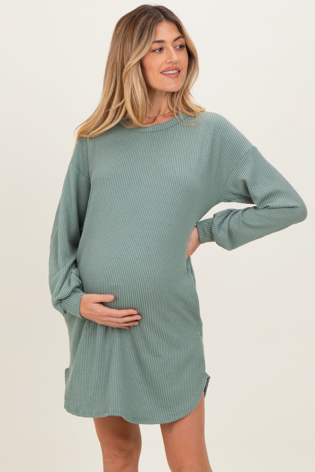 woman wearing a green ribbed long sleeve maternity dress and cradling her baby bump