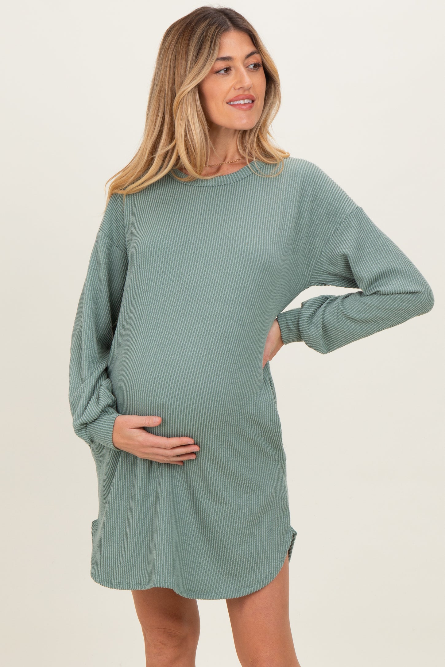 woman wearing a green ribbed long sleeve maternity dress and cradling her baby bump