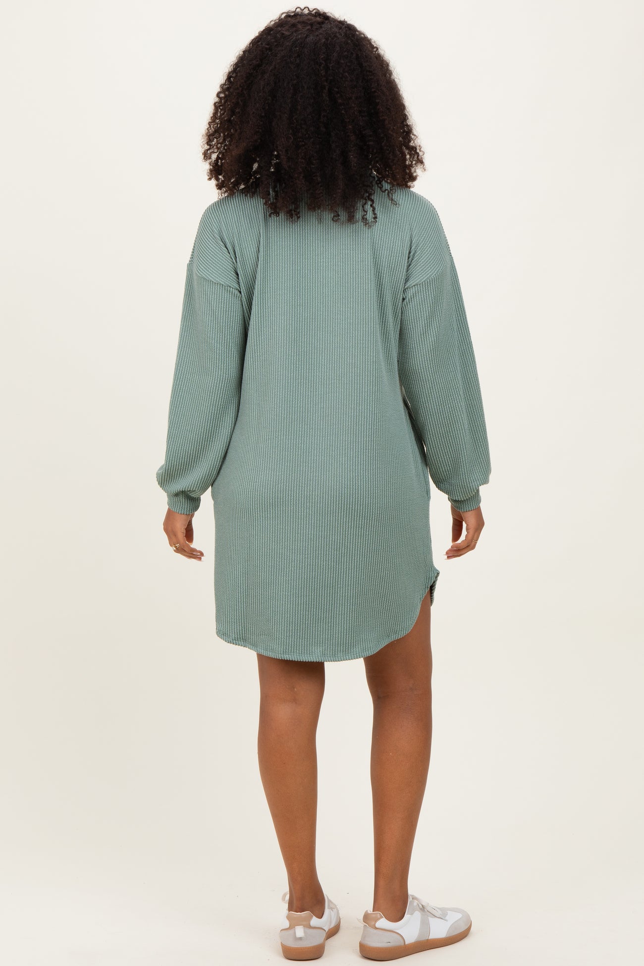 woman wearing a green ribbed long sleeve oversized dress with a high-low hem and white sandals