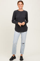 woman wearing a charcoal knit long sleeve top and light blue distressed jeans, standing with hands on hips