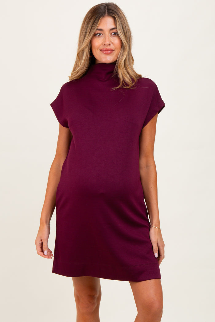 woman wearing a burgundy sleeveless maternity dress with a mock neck and relaxed fit, showing her baby bump