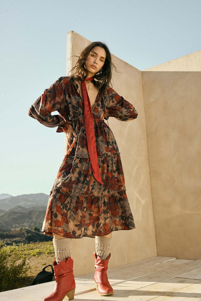 woman wearing a floral long sleeve dress with a tie front and red accents, paired with knee-high boots