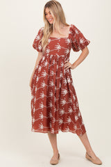 woman wearing a rust-colored midi dress with puff sleeves and a floral pattern