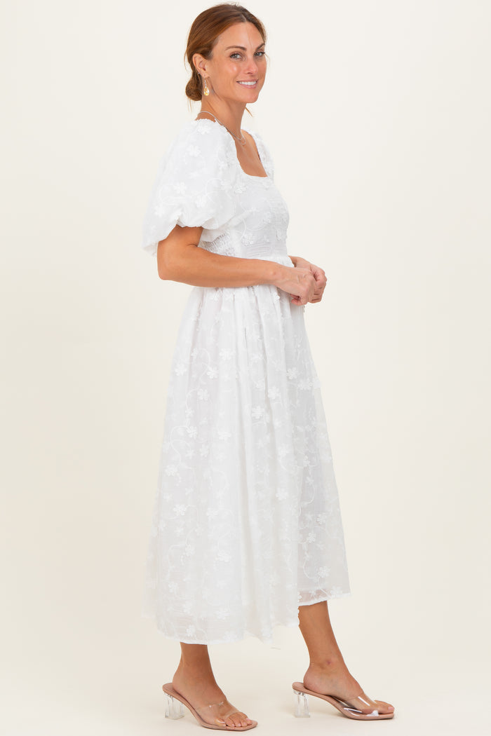 woman wearing a white floral embroidered midi dress with puff sleeves and a square neckline
